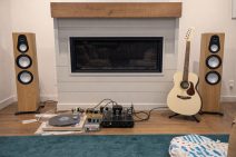 Hemmamiljö med högtalare, vinylspelare och gitarr framför eldstad.